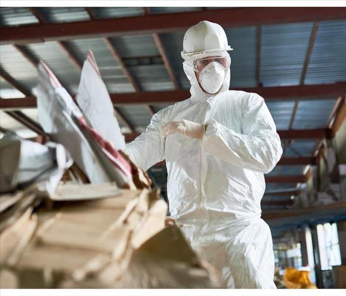 Low angle portrait of factory worker wearing biohazard suit sorting reusable cardboard on waste processing plant