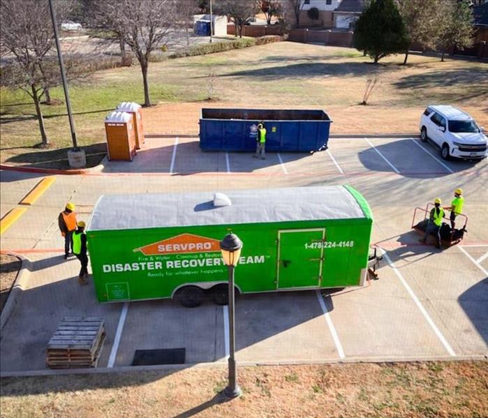 SERVPRO green Disaster Recovery truck trailer parked outside of a property restoration project with four workers around it.